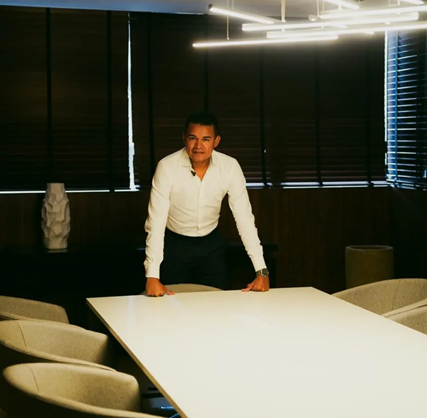 Emanoel Pimentel em uma sala de reunião, apoiado em uma mesa